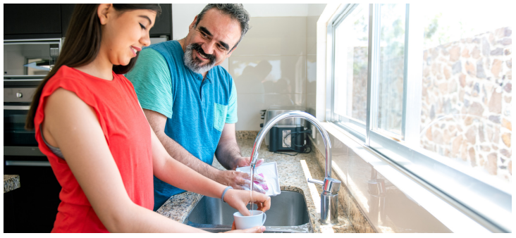 Father in blue shirt helping daughter wash the dishes